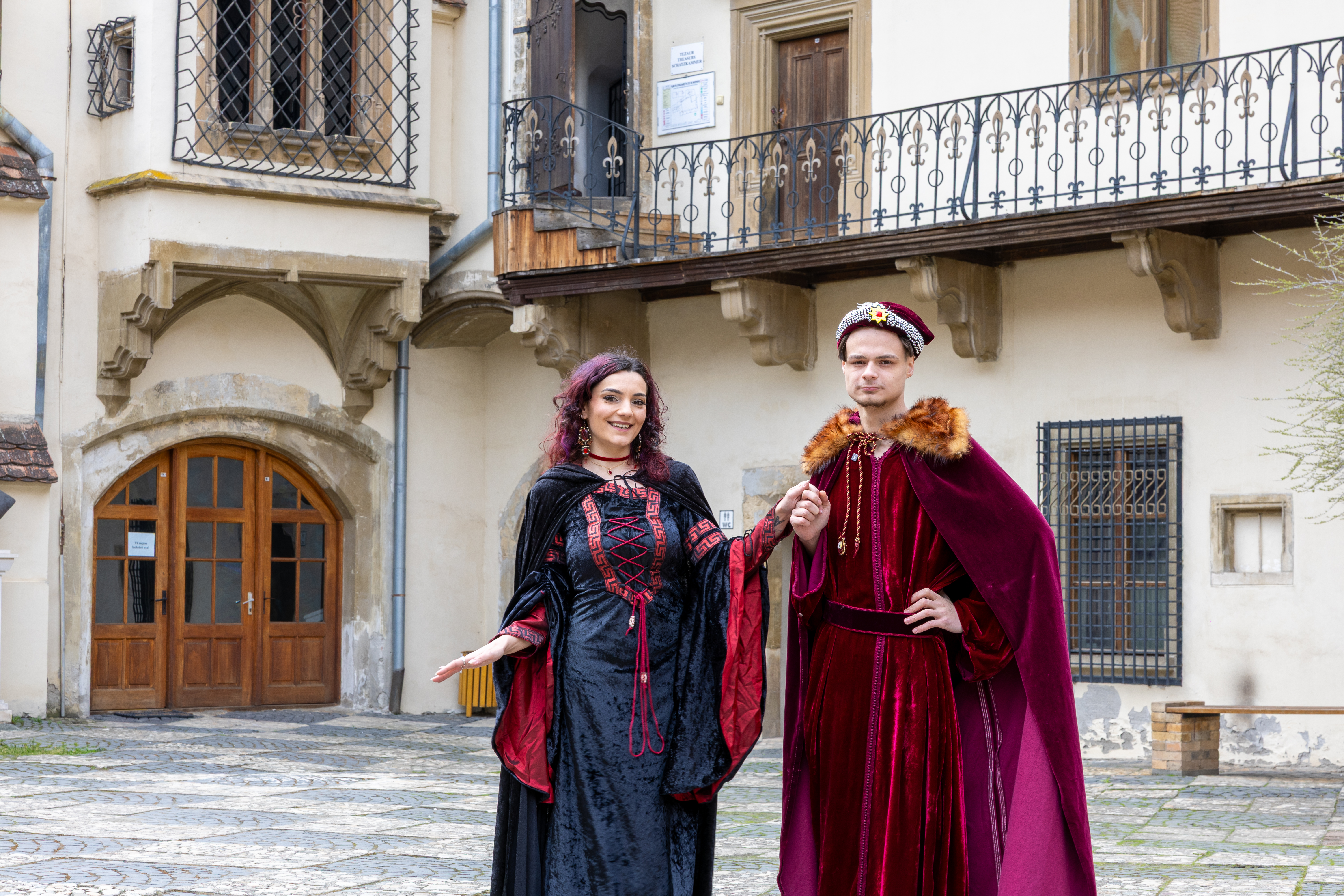 Un jeune couple vêtu de tenues médiévales au premier plan. En arrière -plan la cour du musée de l’histoire. Les deux regardent vers la caméra. La femme semble joyeuse et très fière de son apparence.