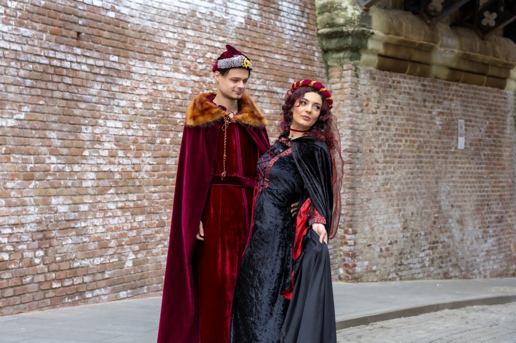 Jeune couple vêtu de tenues médiévales au premier plan. En arrière-plan le Pont des mensonges de Sibiu.