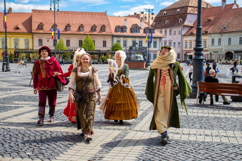 hommes et femmes vêtus en tenues médiévales se promenant dans la Grande Place De Sibiu en Roumanie