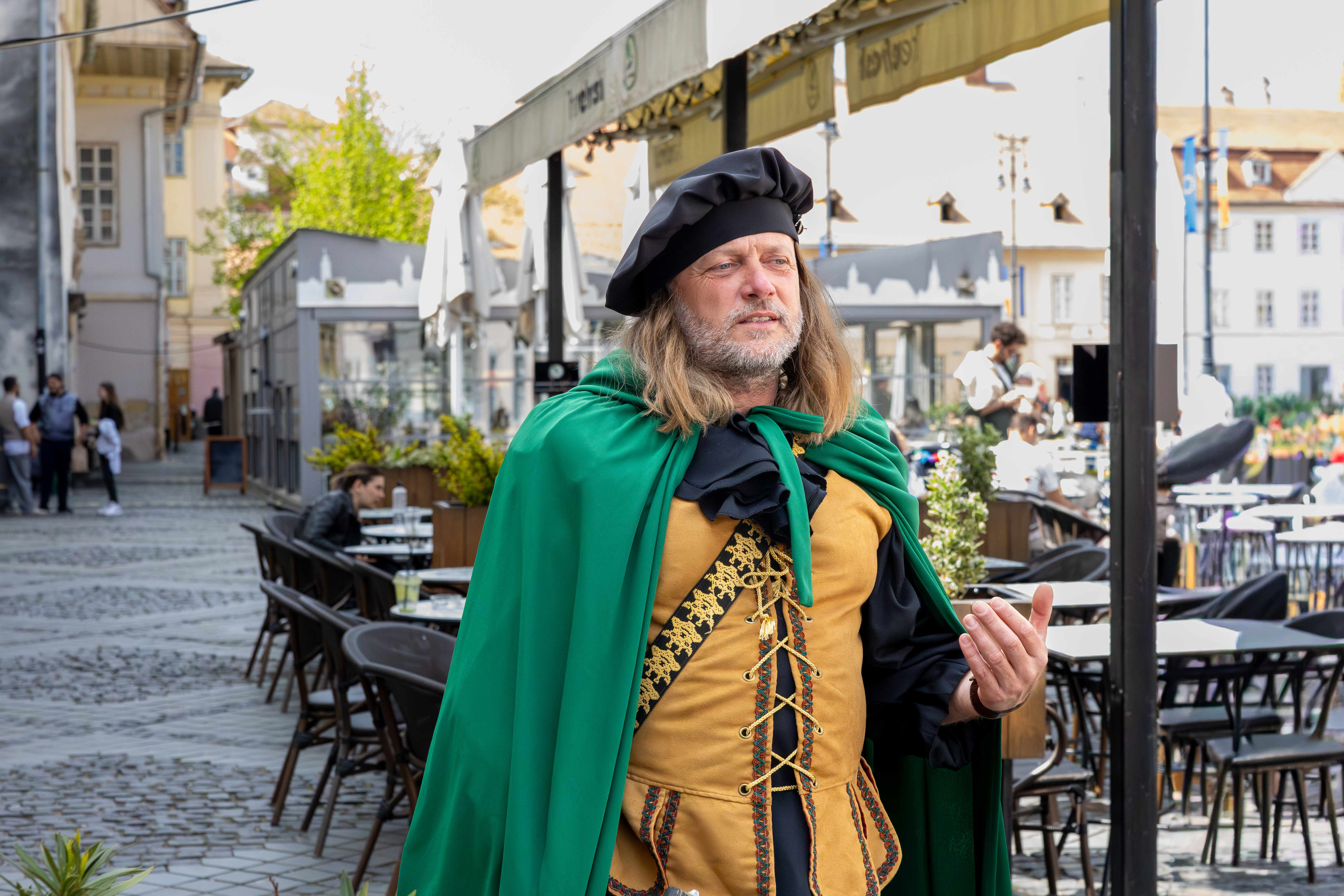 Un troubadour devant une terrasse de la Grande Place de Sibiu. Le geste de sa main nous laisse penser qu’il tente d’expliquer quelque chose d’important.