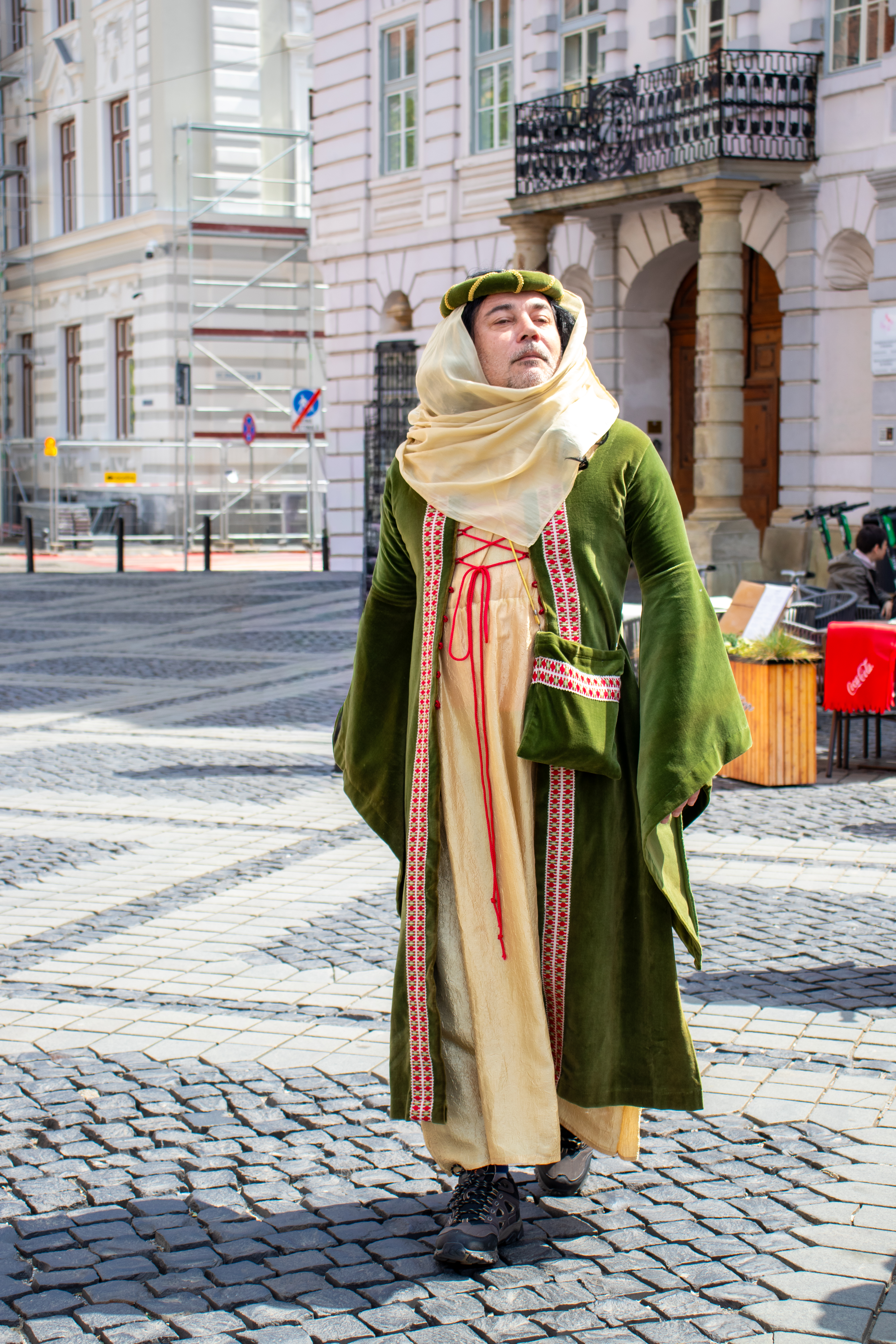 Un homme vêtu en tenue médiévale de femme qui se trouve sur la Grande Place de Sibiu et qui regarde vers la droite très fier de lui et de son apparence.