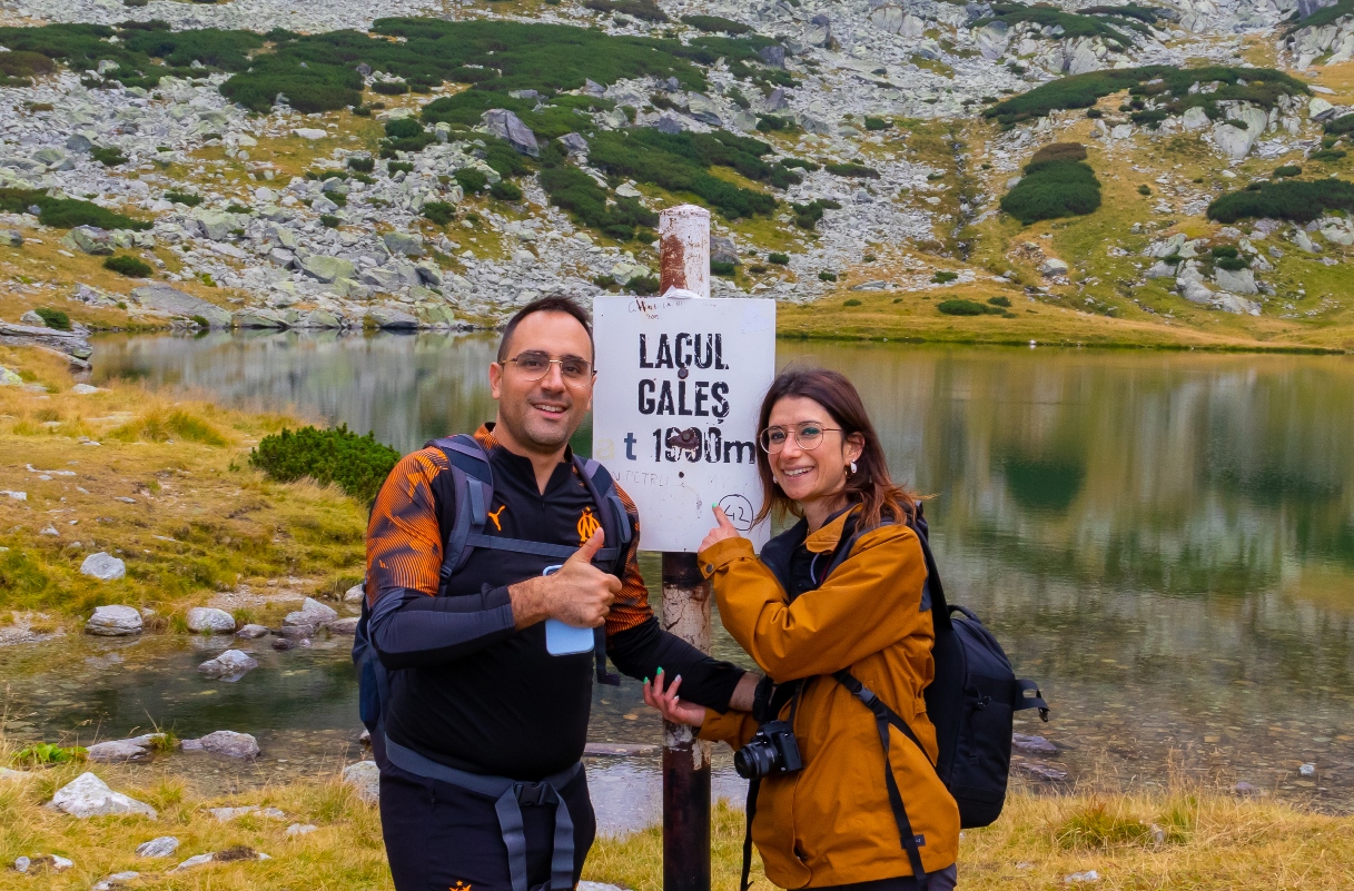 Émeline et Laurent face à la camera, en souriant et montrant Ok avec leurs pouces , avec en arrière-plan le lac Gales.