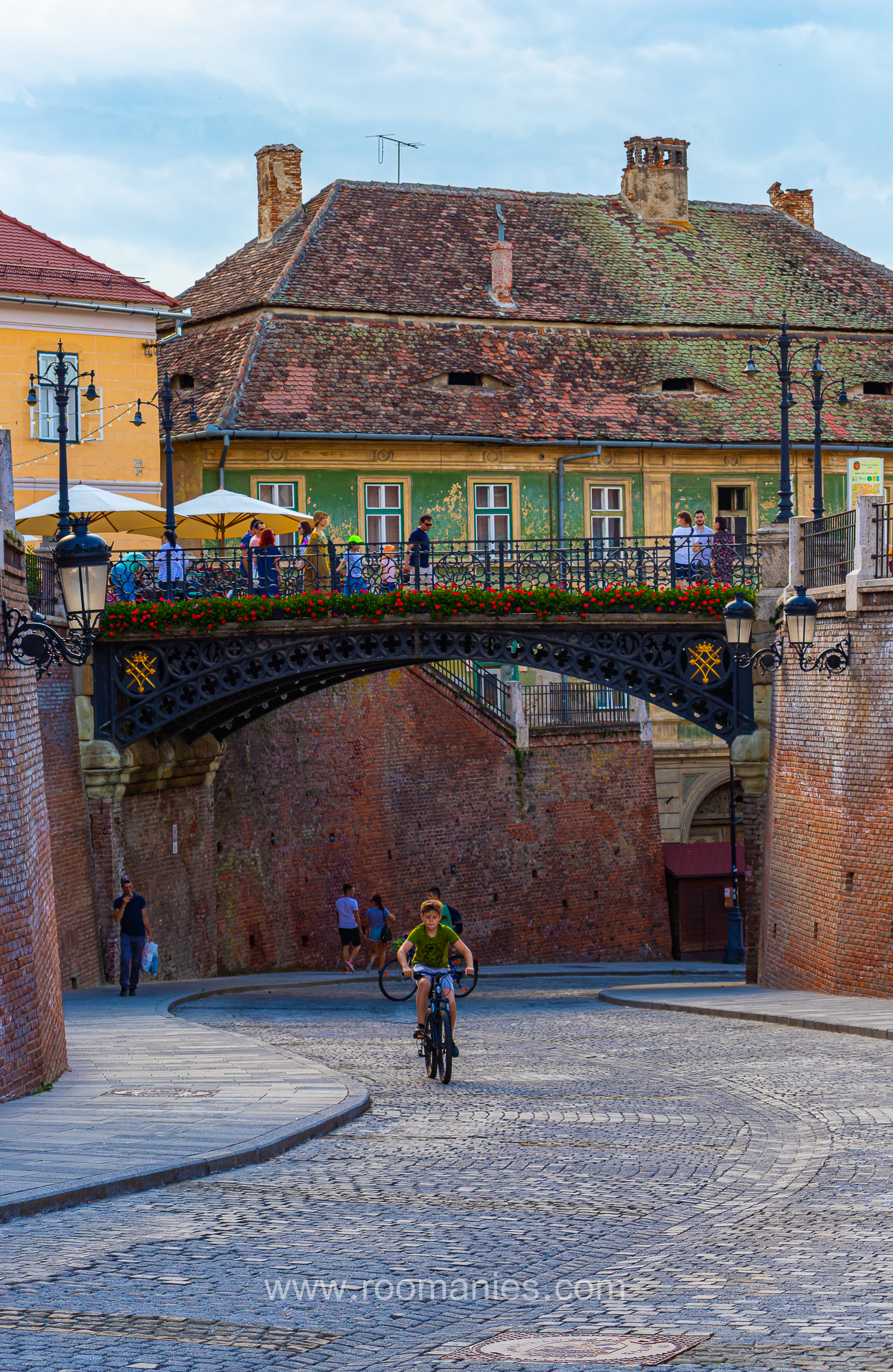Le Pont de Mensonges de Sibiu avec au premier plan un enfant sur une vélo, en arrière-plan quelques maisons médiévales.