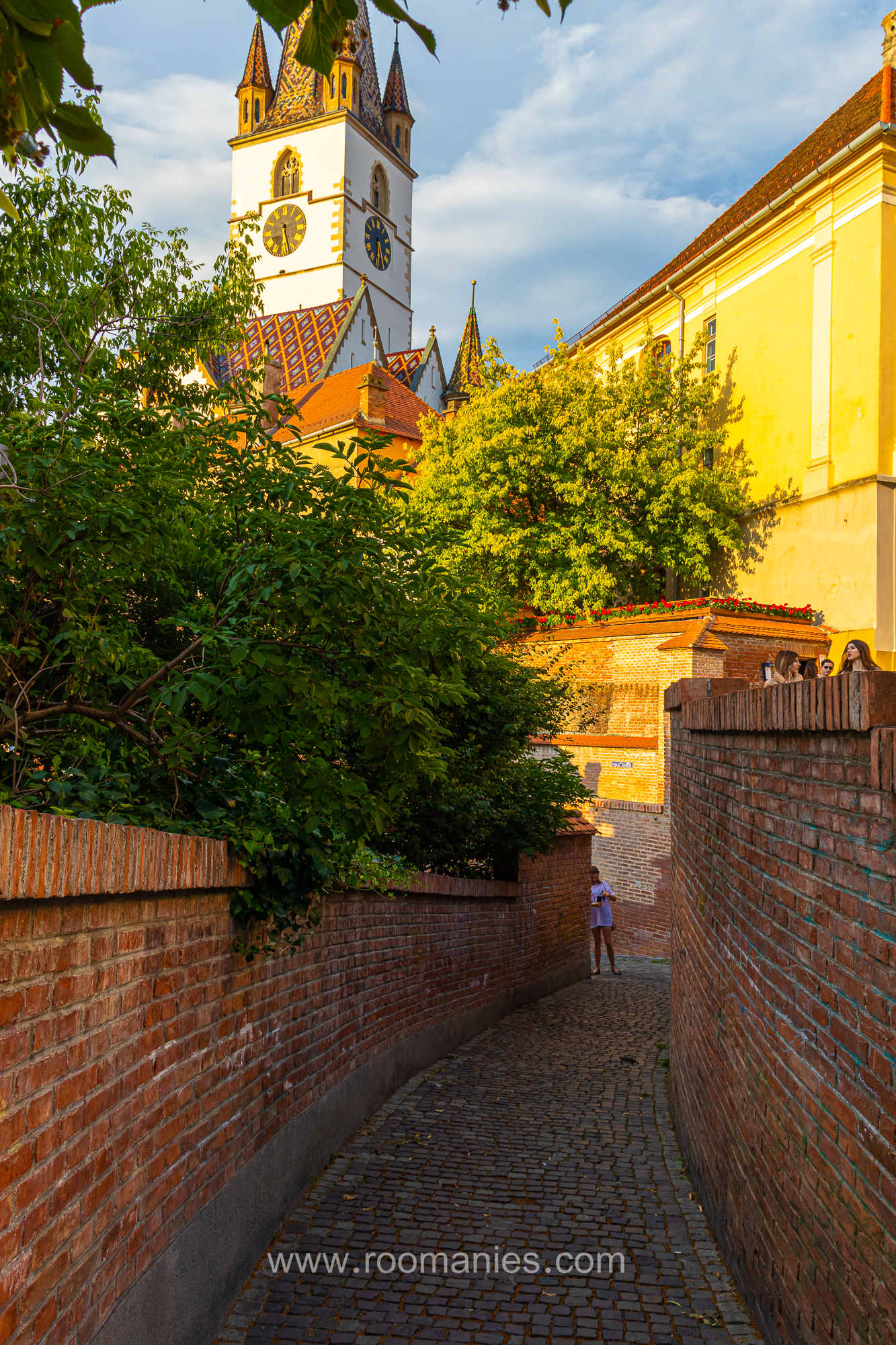 Le Passage des Escaliers de Sibiu, avec au premier plan le petit passage avec ses murs en pierre rouge. En arrière-plan la Cathédrale Evangélique de Sibiu.