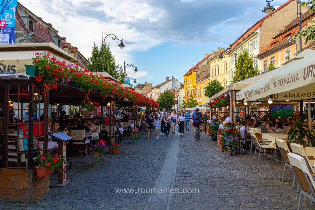 Vue de la rue Nicolae Balcescu de Sibiu avec au premier plan les restaurants et les maisons médiévales de Sibiu, en arrière-plan des passants.  